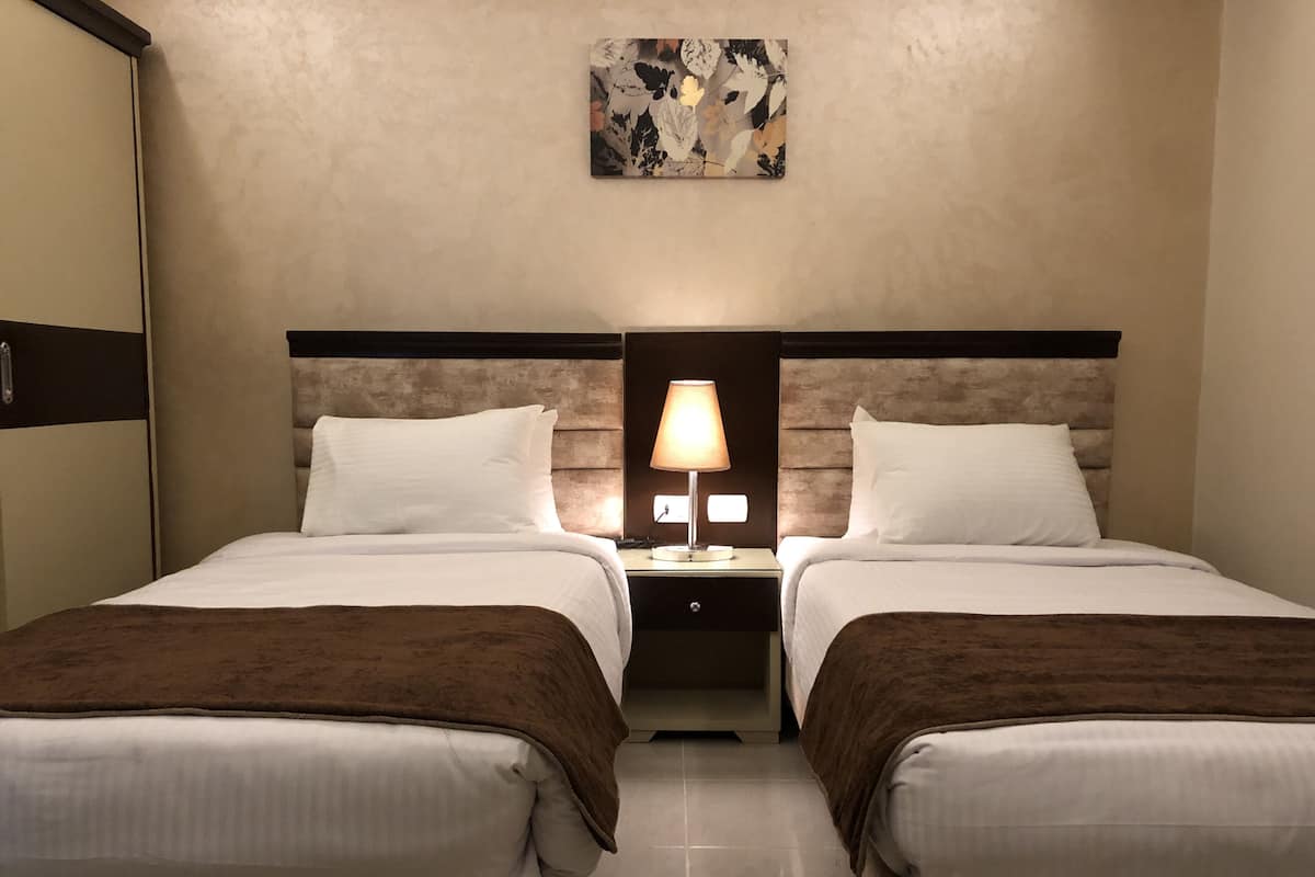A hotel room with two beds, a nightstand with a lamp, a wall-mounted artwork, and a wardrobe.