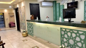 Zona de recepción de un hotel con mostrador, equipo de aire acondicionado, relojes y detalles decorativos.