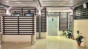 Un pasillo limpio y bien iluminado con un diseño moderno, que presenta una mesa de recepción, una puerta de vidrio con un logotipo y plantas en macetas a lo largo de las paredes.