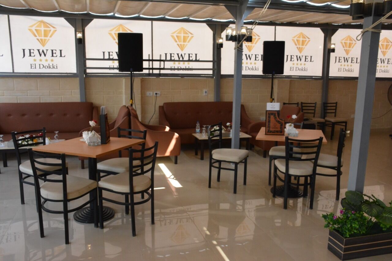 An outdoor seating area with tables and chairs, a sofa, and banners for 'JEWEL El Dokkki'.