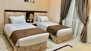 Habitación de hotel con dos camas, una mesita de noche, una lámpara, un cuadro en la pared y una ventana con cortinas.