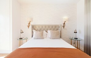 A hotel room with a large bed, two bedside tables, and wall-mounted lamps.