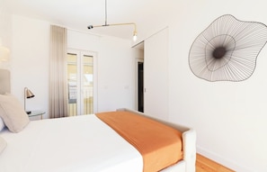 A bedroom with a bed, a bedside lamp, a wall art piece, and a view of the outside.