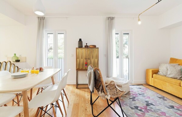A modern living room with a yellow sofa, a dining area with white chairs, and a wooden cabinet.