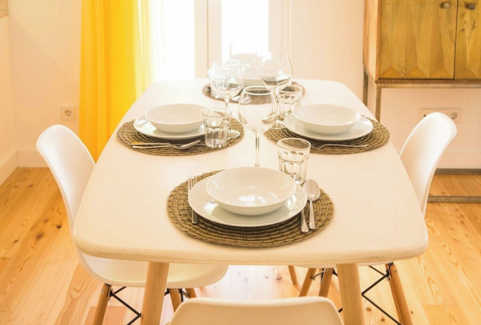 A dining table set with plates, glasses, and cutlery, surrounded by white chairs.