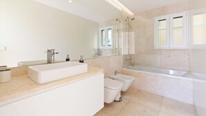 A modern bathroom with a large mirror, a double sink, a toilet, and a bathtub.