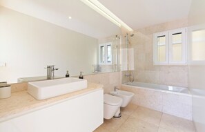 Un baño moderno con un espejo grande, lavamanos doble, inodoro y bañera.
