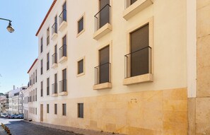 Un edificio de varios pisos con balcones, una calle empedrada y automóviles estacionados.
