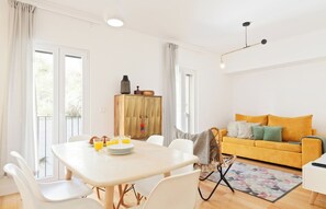Una sala de estar luminosa con un sofá amarillo, una mesa de comedor con sillas y un mueble de madera.