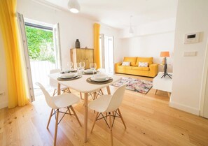 Ein Essbereich mit Tisch für vier Personen, einer Couch und einer TV-Konsole in einem hellen Raum mit Holzboden.