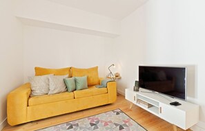 Una sala moderna con un sofá amarillo, un televisor de pantalla plana y un mueble blanco para entretenimiento.