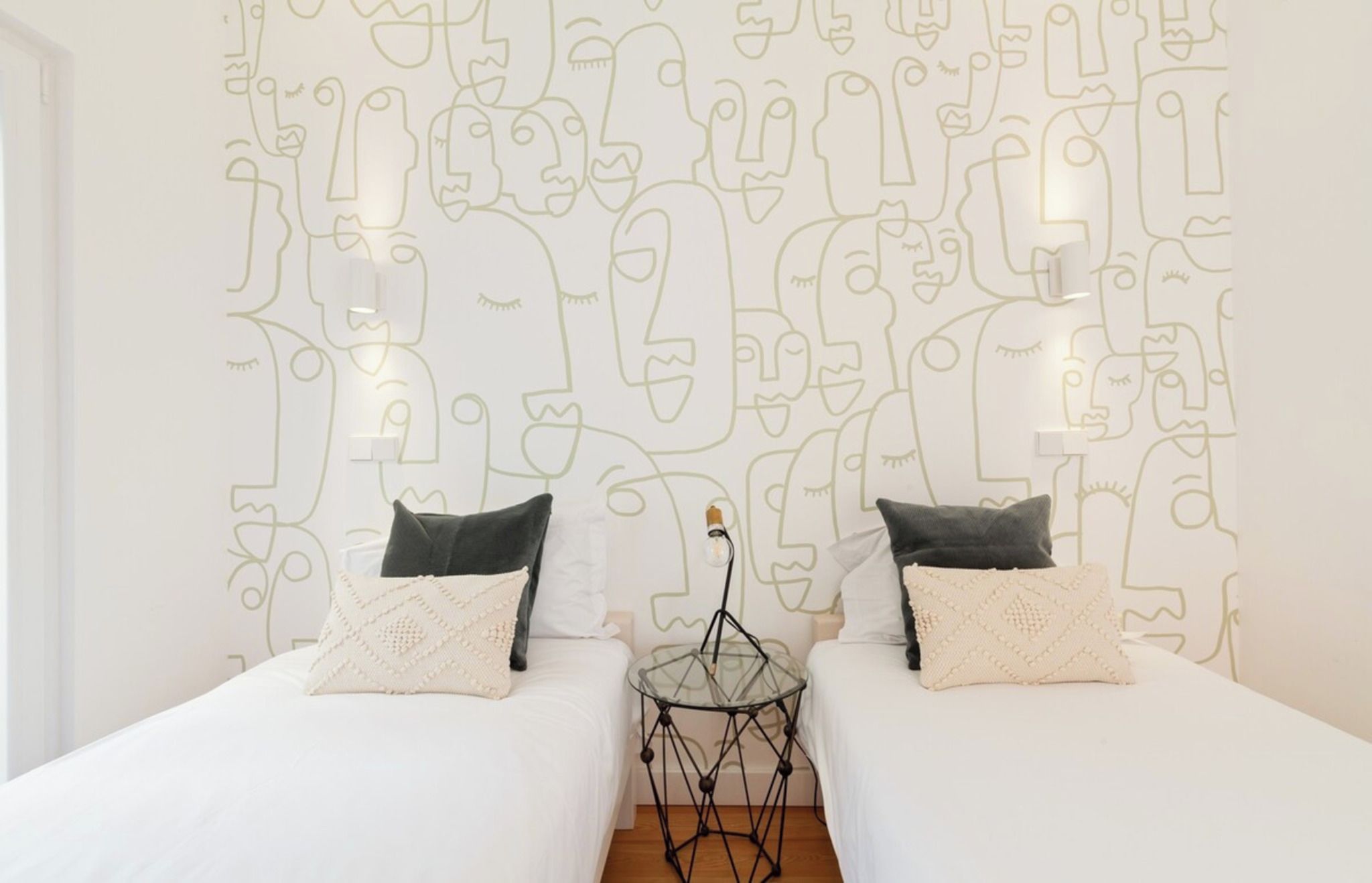 Une chambre d’hôtel avec deux lits, une table d’appoint en verre et un mur orné de dessins abstraits.