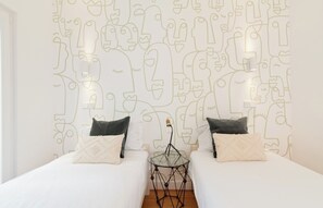 Ein Hotelzimmer mit zwei Betten, einem Glastisch und einer Wand mit abstrakten Linienzeichnungen.