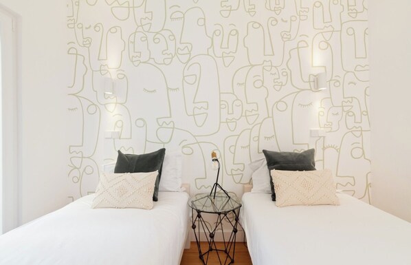 Habitación de hotel con dos camas, una mesita de vidrio y una pared decorada con dibujos lineales abstractos.