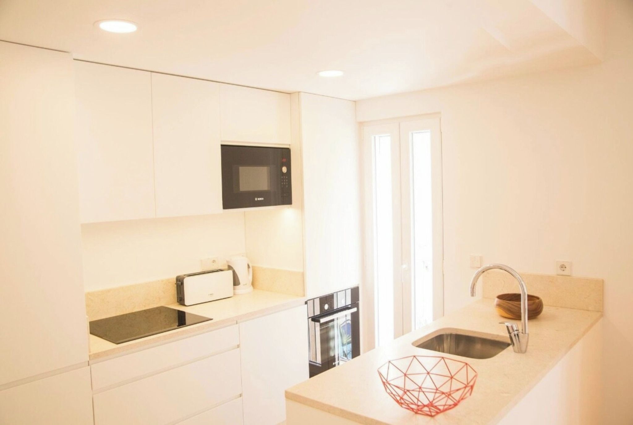 A modern kitchen with a built-in microwave, toaster, oven, and a sink with a wooden bowl.