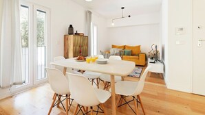 A bright living area with a dining table, chairs, a sofa, and a television.