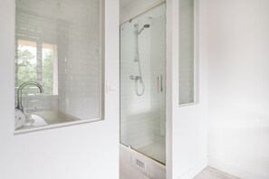 A bathroom with a glass-enclosed shower, a sink with a modern faucet, and a window providing natural light.