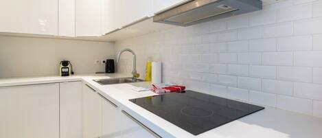 A modern kitchen with white cabinets, a black induction cooktop, a stainless steel sink, and a range hood.