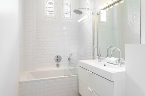 A modern bathroom with white subway tiles, a glass-enclosed shower, a white bathtub, and a vanity with a mirror.