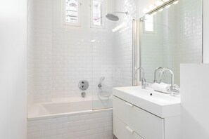 A modern bathroom with white subway tiles, a glass-enclosed shower, a white bathtub, and a vanity with a mirror.