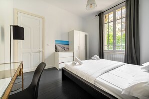A hotel room with a bed, a desk, a chair, a wardrobe, and a painting on the wall.