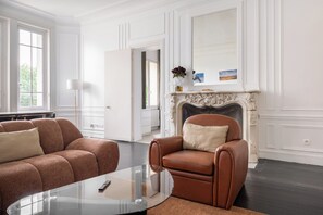 A living room with a fireplace, two leather armchairs, a glass coffee table, and a white door leading to another room.