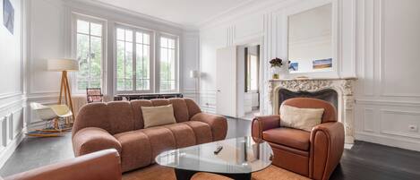 A spacious living room with a large sofa, a glass coffee table, and a fireplace.