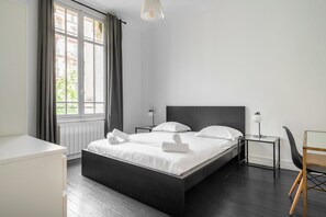 A modern bedroom with a large bed, bedside tables, a chair, and a view of the city through a window.