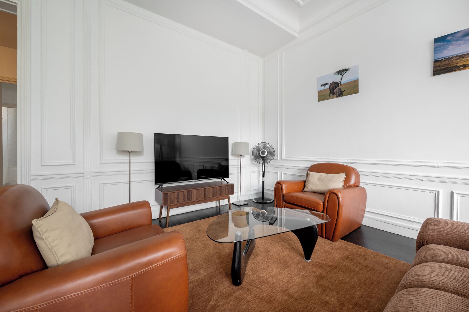 A modern living room with a leather sofa, a glass coffee table, a TV, and a floor lamp.