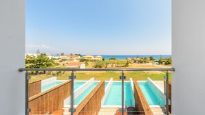 A pool area with multiple lanes, a wooden deck, and a view of the sea and distant buildings. - Belussi Exclusive Suites - Adults Only (Zakynthos)