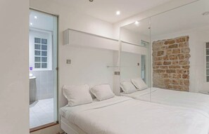 A modern bedroom with a large bed, a glass shower enclosure, and a stone wall. - The Modern Eiffel 2BDR Stay in Paris Center (Paris)