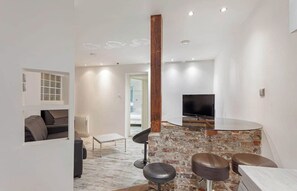 A modern living room with a TV, seating area, and a kitchen counter. - The Modern Eiffel 2BDR Stay in Paris Center (Paris)