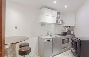 A compact kitchen with a built-in oven, microwave, and a dishwasher. There are stools at a small table, and a refrigerator is visible. - The Modern Eiffel 2BDR Stay in Paris Center (Paris)