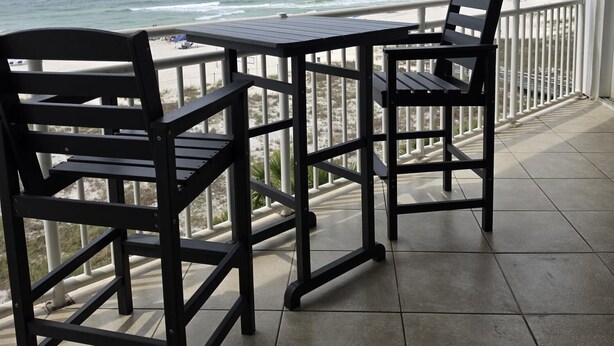 En balkon med udsigt over havet, to stole og et bord.