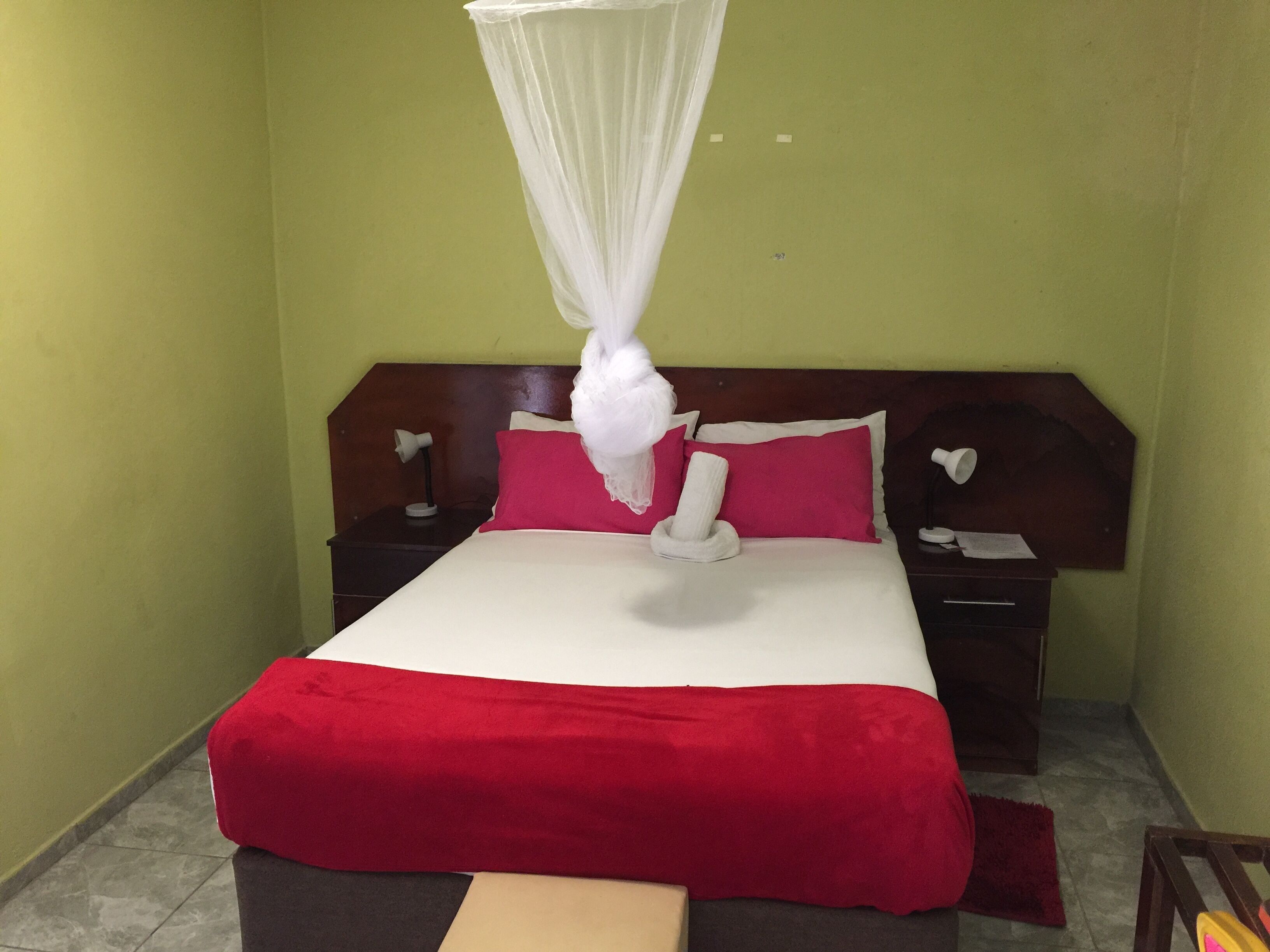 A hotel room with a bed, a nightstand, a bedside table, a lamp, and a red blanket.