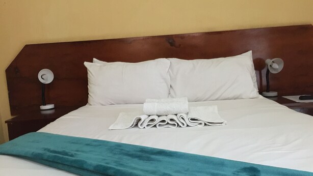 A neatly made bed with white linens, a teal throw blanket, and rolled towels on the bed.