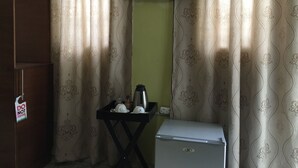 A small room with a refrigerator, a table with a kettle and cups, a TV on the wall, and curtains with a pattern.
