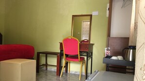 A room with a red sofa, a small table, a chair, a mirror, a refrigerator, and a kettle on a shelf.