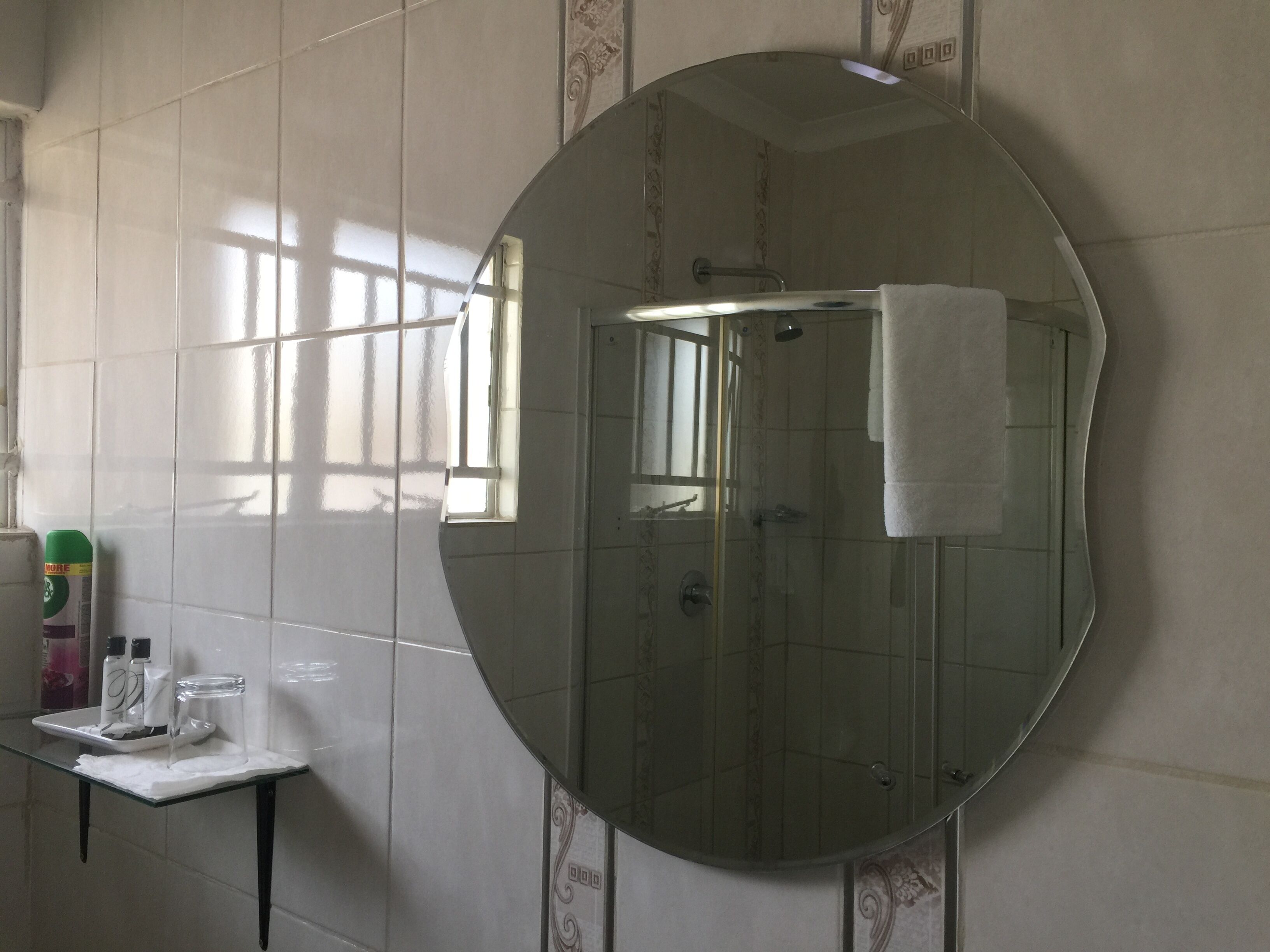 Un baño con un espejo grande, una cabina de ducha de vidrio y una mesita con artículos de aseo.