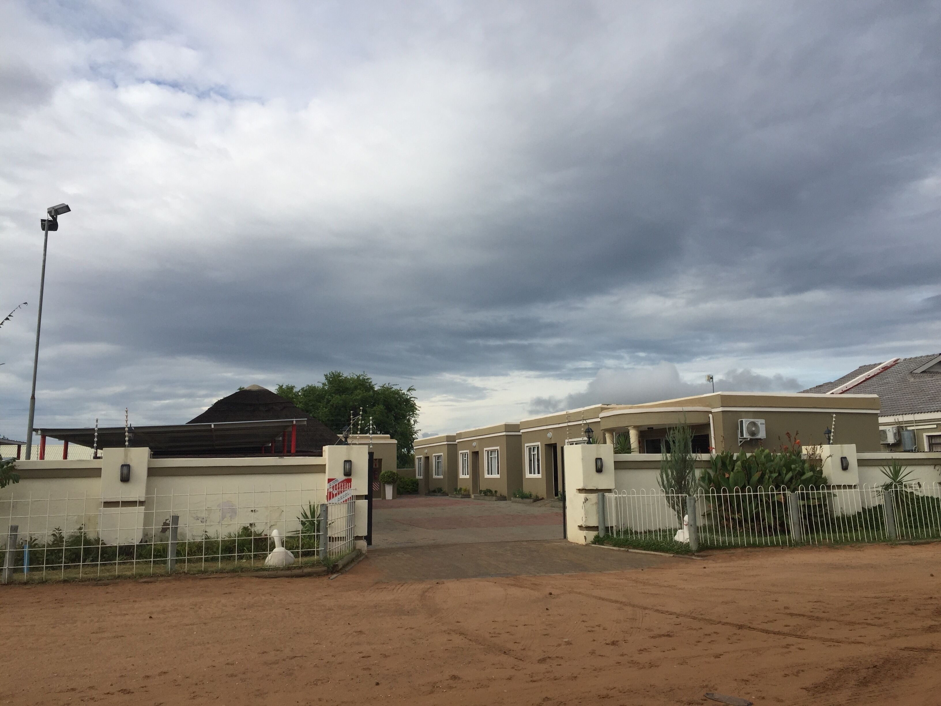 A gated residential area with multiple houses, a dirt road, and a cloudy sky.