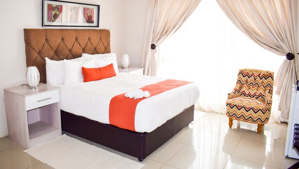 A neatly arranged hotel room with a large bed, a bedside table, a chair, and a window with curtains. - Royal Court Guest House (Letlhakane)