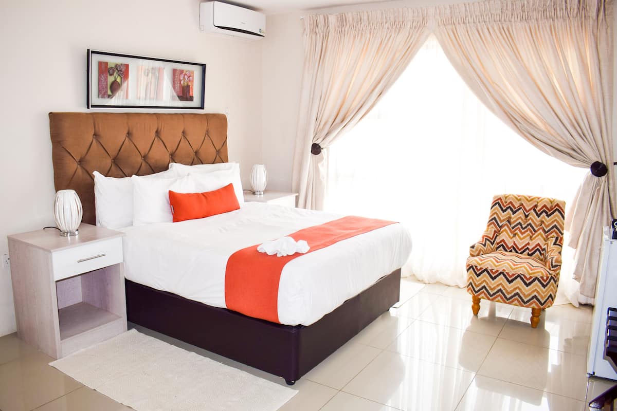 A neatly arranged hotel room with a large bed, a bedside table, a chair, and a window with curtains.