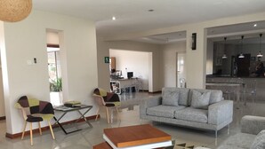 A spacious living area with a grey sofa, a coffee table with a book, and a patterned rug. - Royal Court Guest House (Letlhakane)