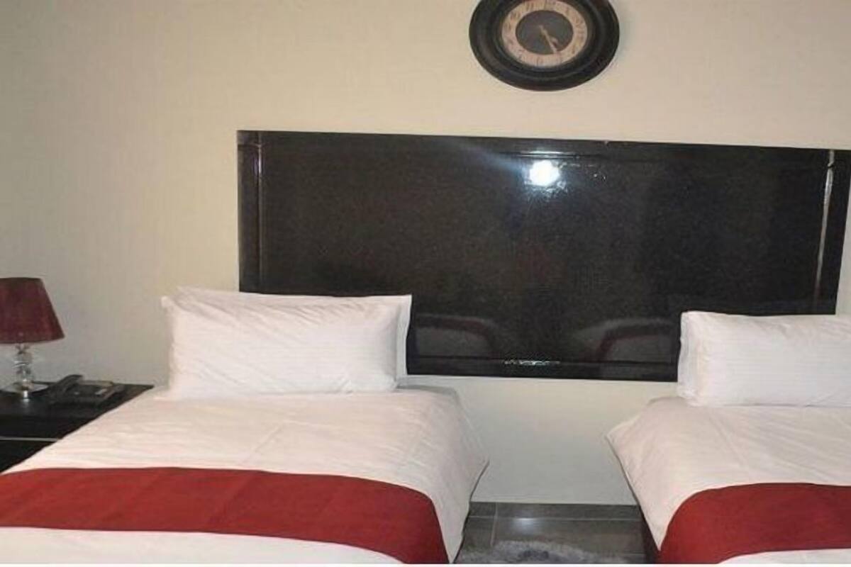 A hotel room with two beds, a large flat-screen TV mounted on the wall, and two bedside tables with lamps.
