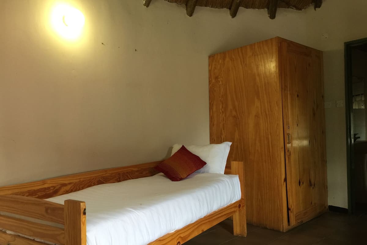 A wooden bed with white bedding and a red pillow in a room with a wooden wardrobe and a light fixture on the wall.