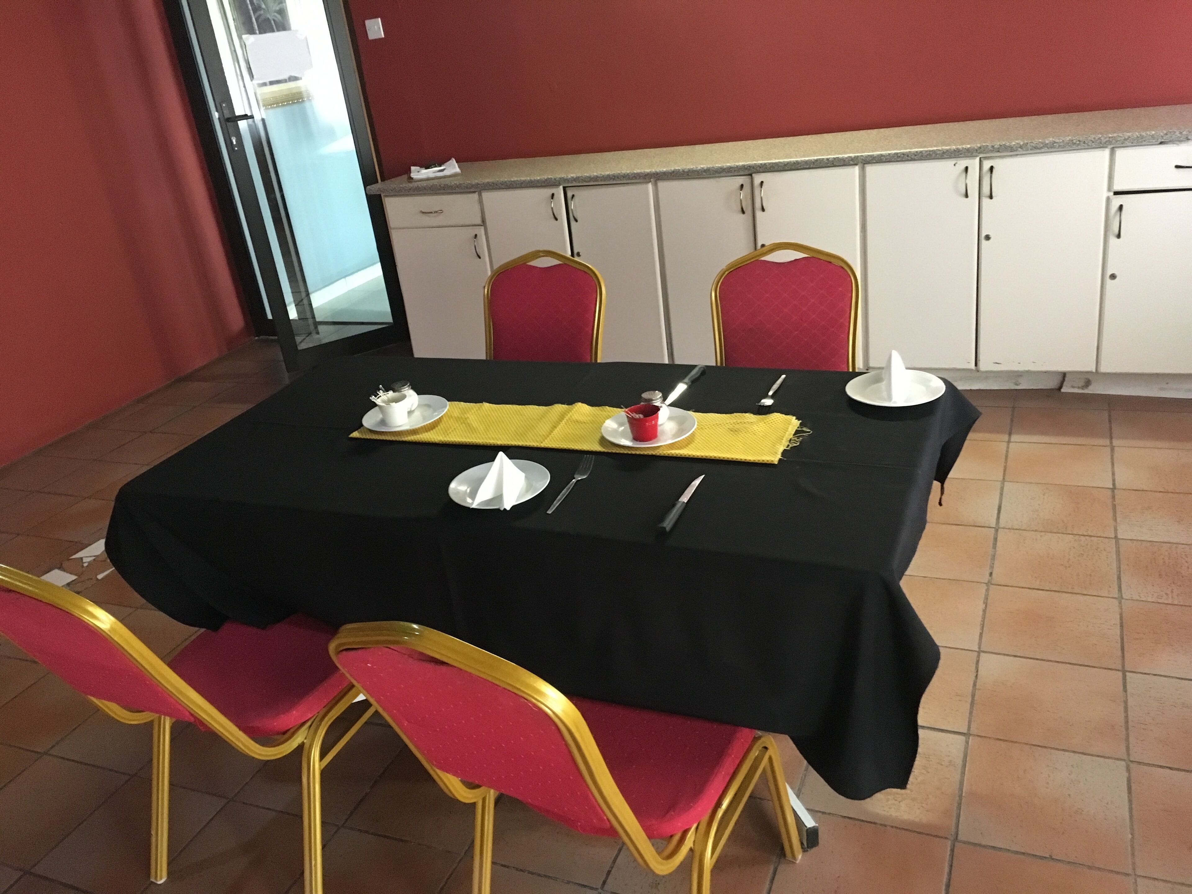 Un comedor con mantel negro, sillas rojas y camino de mesa amarillo.