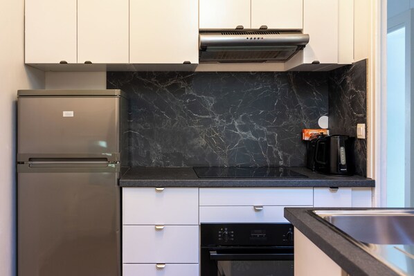 A modern kitchen with a built-in refrigerator, a black marble backsplash, and a coffee maker on the countertop.