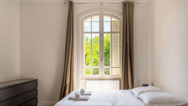 A bedroom with a bed, a dresser, and a window with curtains.