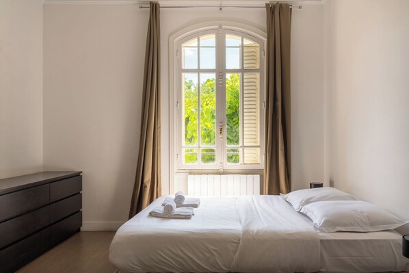 A bedroom with a bed, a dresser, and a window with curtains.