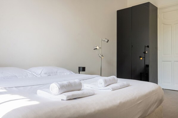 Une chambre d’hôtel avec un grand lit, une armoire sombre et une lampe sur pied.